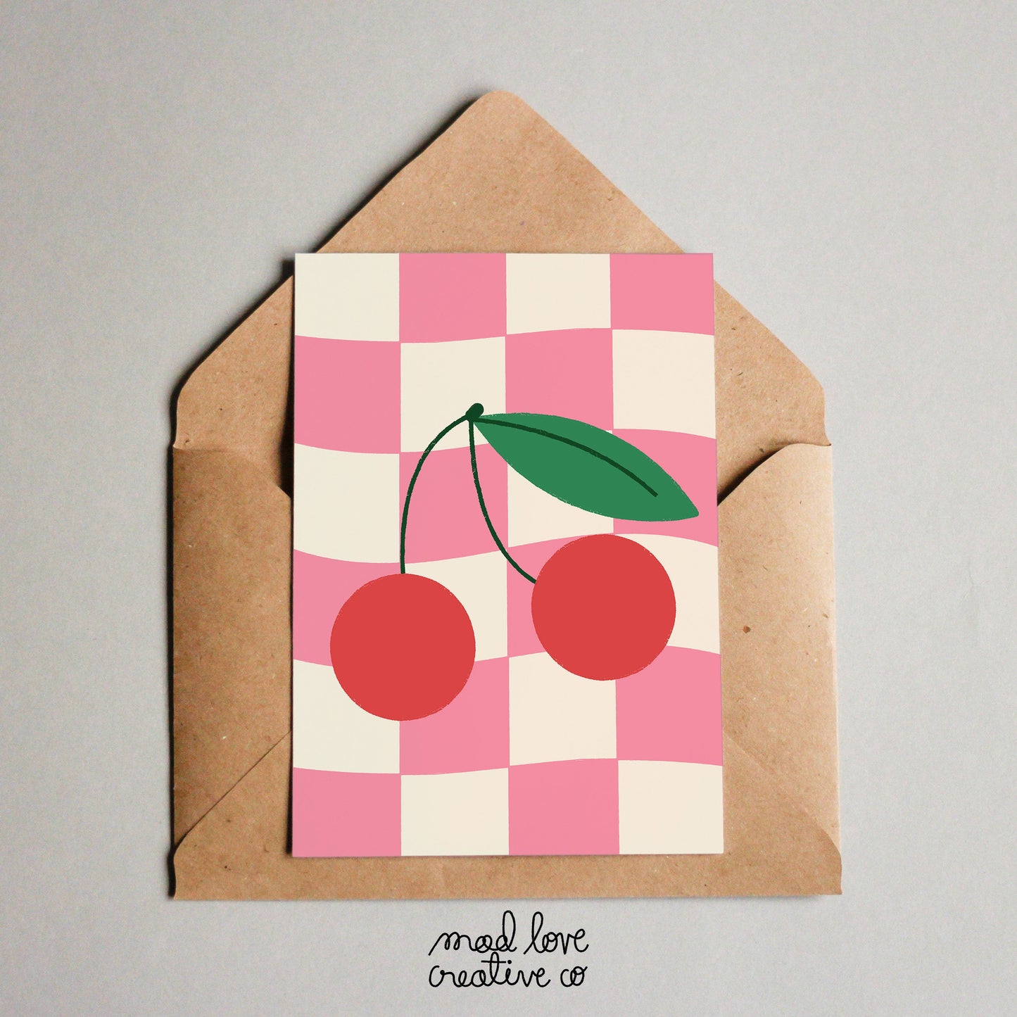 Cute card featuring a pair of cherries on a pink checkered background. Made in Canada by Mad Love Creative Co.