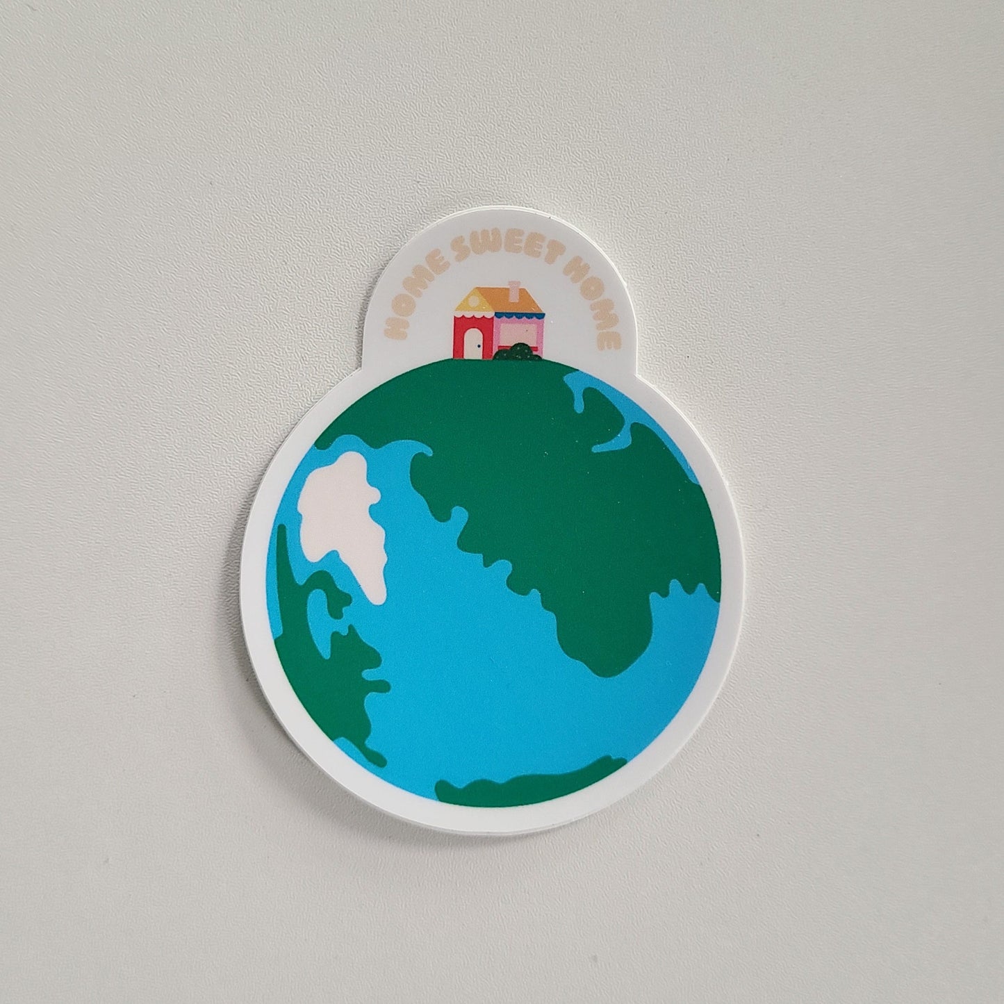 Home Sweet Home sticker featuring a home sitting on top of an illustration of earth. Made in Canada by Mad Love Creative Co.