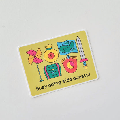 Sticker with colorful icons and text 'busy doing side quests!' on a light gray background