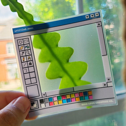 Hand holding a transparent sticker with a digital interface design, showing a leaf shadow on a screen.