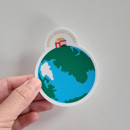Home Sweet Home sticker featuring a home sitting on top of an illustration of earth. Made in Canada by Mad Love Creative Co. 