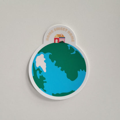 Home Sweet Home sticker featuring a home sitting on top of an illustration of earth. Made in Canada by Mad Love Creative Co. 