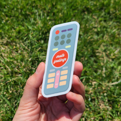 "Mute Feelings" sticker shaped like a TV remote. Made in Canada by Mad Love Creative Co. 