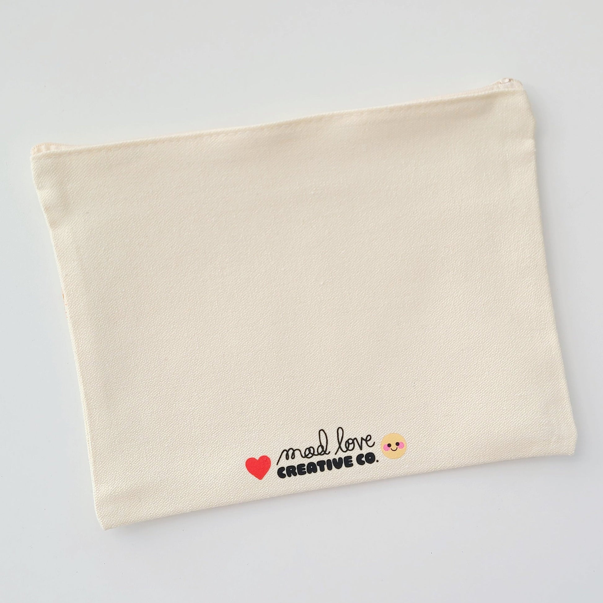 Beige pouch with 'mad love creative co.' text on a grey background