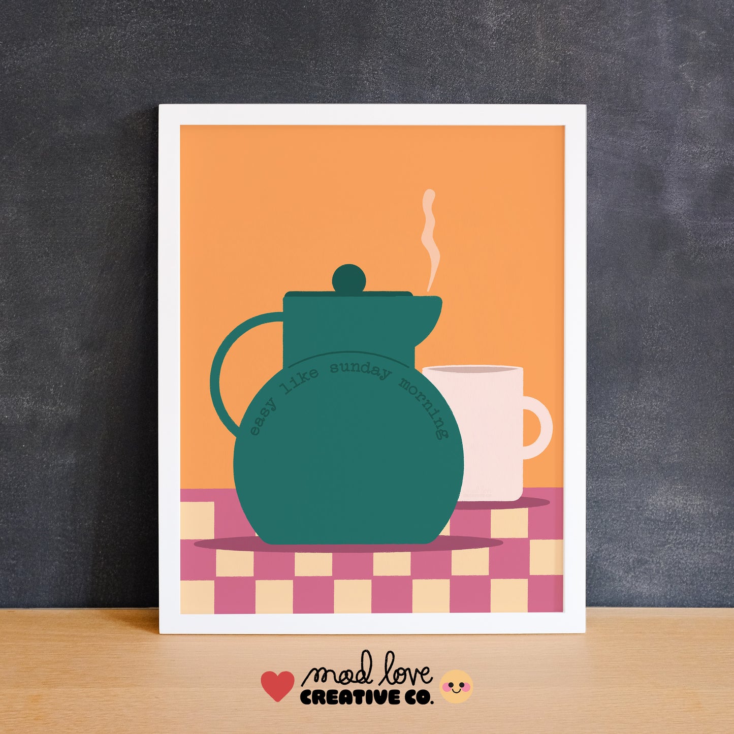Framed artwork of a teal teapot and white mug on a checkered tablecloth with an orange background with the text "easy like Sunday morning". Made in Canada by Mad Love Creative Co. 