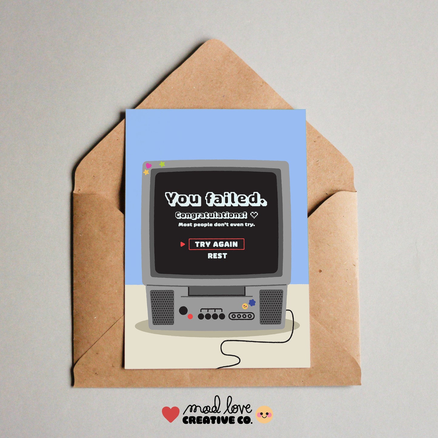 Card with retro computer graphic and envelope on a gray background. Card has the text "you failed, congratulations". Made in Canada by Mad Love Creative Co. 